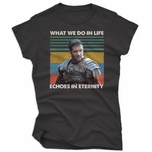 May include: Black t-shirt featuring a movie still with a man in armor and the text "WHAT WE DO IN LIFE ECHOES IN ETERNITY" in white. The design includes horizontal stripes in green, yellow, and blue.