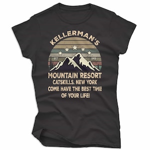 May include: Dark gray t-shirt featuring a retro design with the text "KELLERMAN'S MOUNTAIN RESORT CATSKILLS, NEW YORK". The design includes a mountain range, stars, and the year 1963.