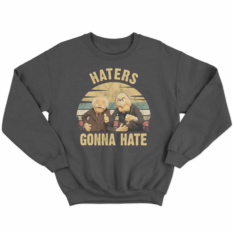May include: Dark gray sweatshirt featuring a graphic of two puppet characters with the text "HATERS GONNA HATE" in a vintage style. The design includes a retro sunset background.