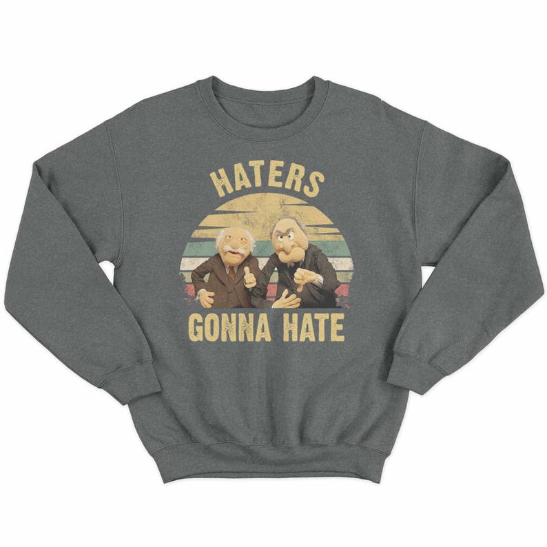 May include: A dark gray sweatshirt featuring a graphic of two Muppet characters with the text "HATERS GONNA HATE" in a vintage style. The design includes a sunset-like background with horizontal stripes.