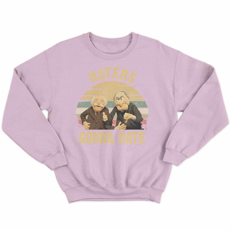 May include: A light purple sweatshirt featuring a graphic of two Muppet characters with the text "HATERS GONNA HATE" in yellow. The graphic includes a sunset design in the background.