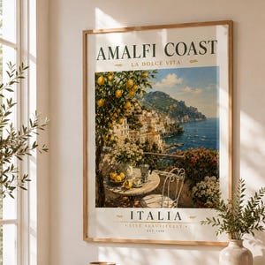May include: A framed print of the Amalfi Coast in Italy, with the text "AMALFI COAST LA DOLCE VITA" at the top and "ITALIA LIVE BEAUTIFULLY EST. 1959" at the bottom. The print is displayed above a wooden bench with a basket and books.