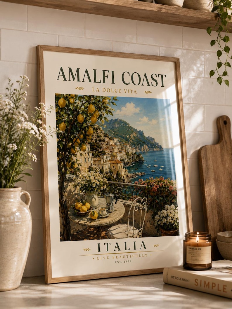 May include: A framed print featuring the Amalfi Coast in Italy. The artwork depicts a scenic view of a coastal town with a lemon tree, a table set for coffee, and the text "AMALFI COAST" and "ITALIA". The print is in a wooden frame.