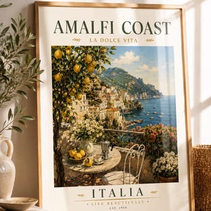 May include: Framed art print featuring a scenic view of the Amalfi Coast in Italy. The artwork depicts a coastal town with colorful buildings, a table with lemons and coffee, and the text "AMALFI COAST" and "ITALIA".
