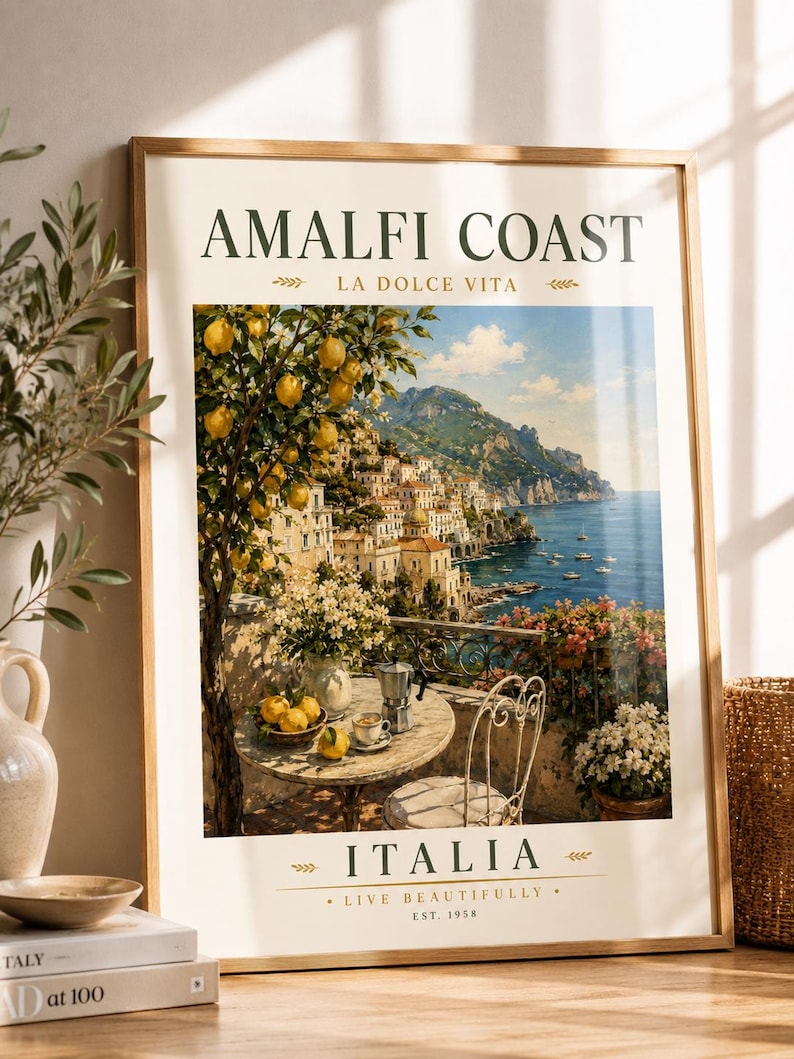 May include: Framed art print featuring a scenic view of the Amalfi Coast in Italy. The artwork depicts a coastal town with colorful buildings, a table with lemons and coffee, and the text "AMALFI COAST" and "ITALIA".