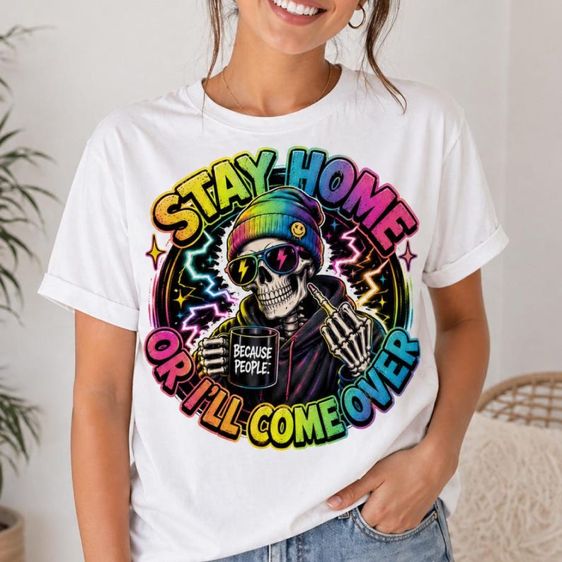 May include: White t-shirt with a colorful graphic of a skeleton wearing sunglasses and a rainbow beanie. The skeleton holds a mug that says "BECAUSE PEOPLE" and gives the middle finger. The text "STAY HOME OR I'LL COME OVER" is also on the shirt.