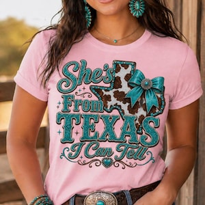 Puede incluir: Camiseta rosa con el texto "She's From Texas I Can Tell". El dise&ntilde;o incluye un gr&aacute;fico en forma de Texas con un estampado de piel de vaca y un lazo turquesa. El texto y los acentos son de purpurina turquesa.