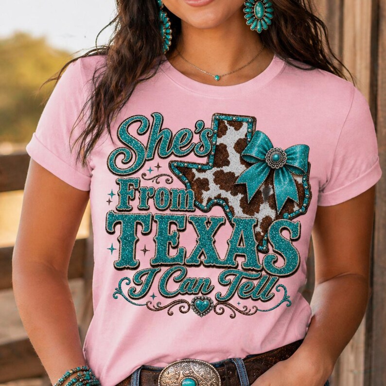 Puede incluir: Camiseta rosa con el texto "She's From Texas I Can Tell". El dise&ntilde;o incluye un gr&aacute;fico en forma de Texas con un estampado de piel de vaca y un lazo turquesa. El texto y los acentos son de purpurina turquesa.