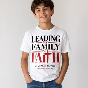 Peut inclure: T-shirt blanc avec l'inscription "LEADING MY FAMILY BY FAITH" en noir et rouge. Le t-shirt comprend une croix rouge et le verset biblique Josu&eacute; 24:15. Le t-shirt est port&eacute; par une personne.