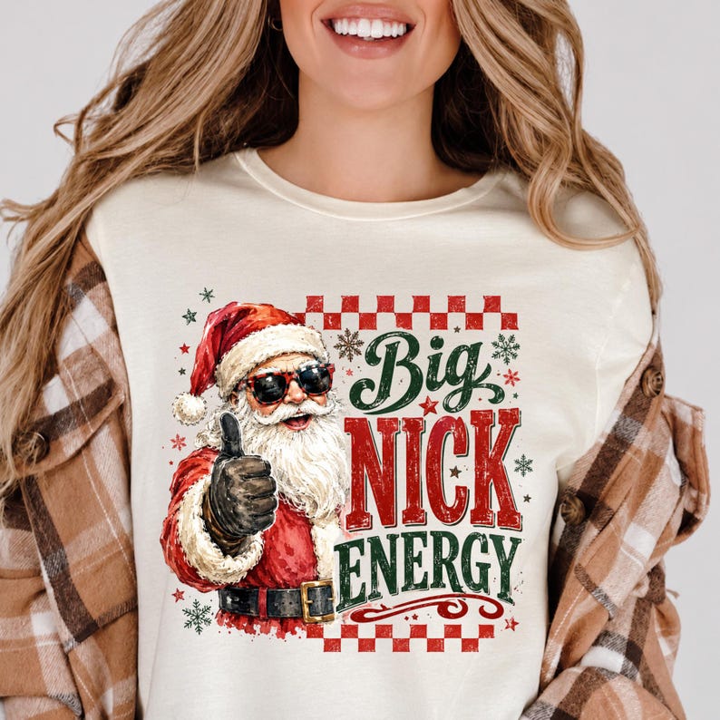 Peut inclure: Un t-shirt couleur cr&egrave;me avec une illustration du P&egrave;re No&euml;l portant des lunettes de soleil et faisant un pouce lev&eacute;. Le texte Big Nick Energy est &eacute;crit en rouge et vert, entour&eacute; d'une bordure &agrave; carreaux rouges et de petits flocons.