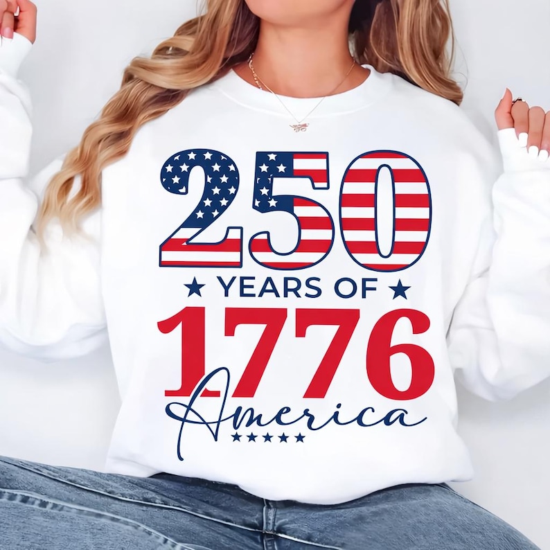 May include: White sweatshirt with a patriotic design. The design features the number "250" in red and blue, with stars and stripes, and the text "YEARS OF 1776 America" in red and blue.