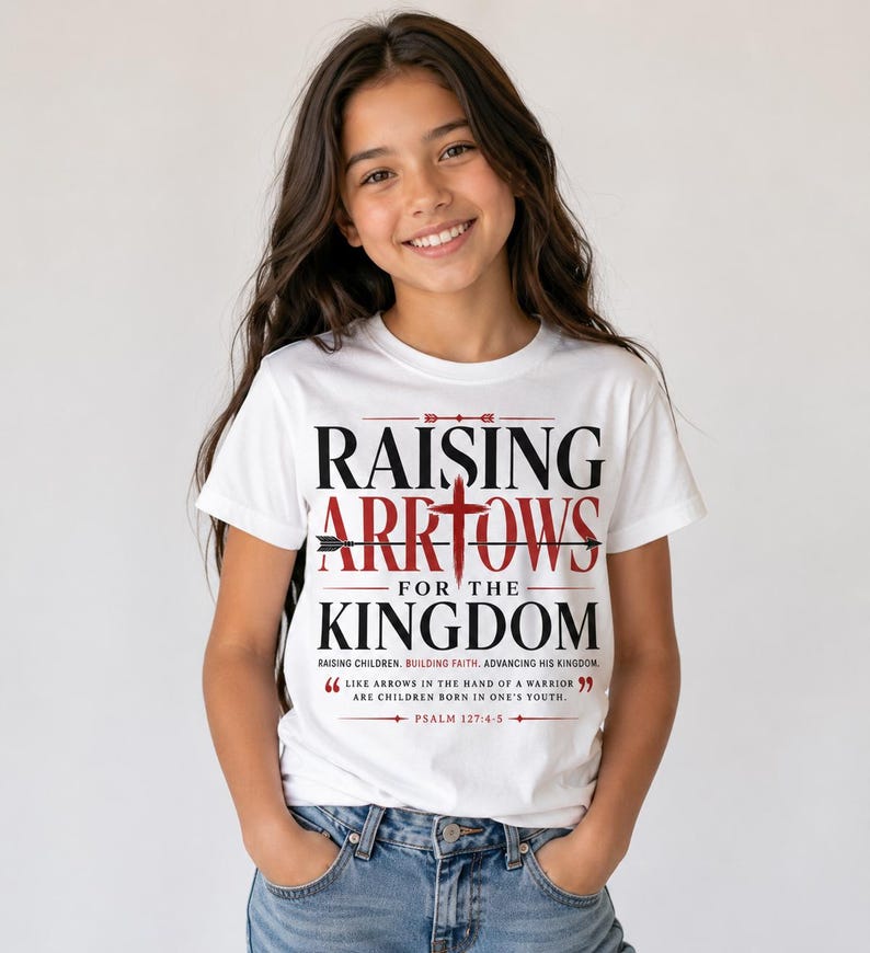 Peut inclure: Un t-shirt blanc avec l'inscription "RAISING ARROWS FOR THE KINGDOM" en noir et rouge. Le t-shirt comprend &eacute;galement une citation du Psaume 127:4-5. Port&eacute; par une personne aux cheveux bruns et un jean bleu.