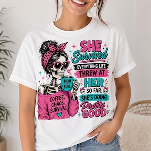 May include: White t-shirt with a skeleton graphic wearing sunglasses and a pink headband, holding a coffee mug. Text reads "SHE Survived" and "Coffee. Chaos. Survival."