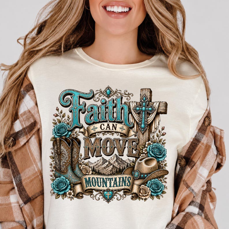 May include: A cream-coloured t-shirt featuring a graphic print with the text "Faith Can Move Mountains." The design includes a cross, cowboy boots, a cowboy hat, mountain peaks, and turquoise-coloured roses, all rendered in shades of brown and blue.