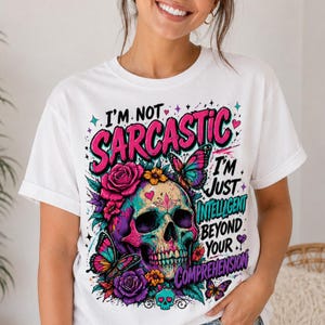 May include: White t-shirt with a colorful skull graphic. The skull is decorated with flowers and butterflies, and the text reads "I'M NOT SARCASTIC I'M JUST INTELLIGENT BEYOND YOUR COMPREHENSION."