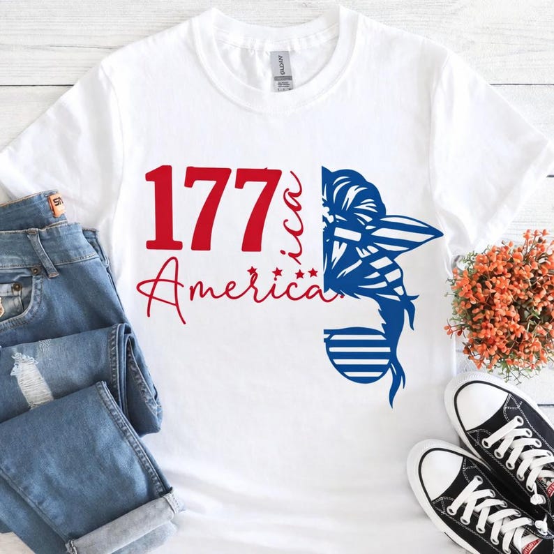 May include: White t-shirt with the text "1776 America" in red script and a blue and white graphic. The shirt is paired with blue jeans and black canvas sneakers with white soles.