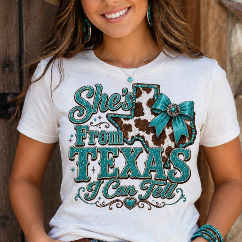 Puede incluir: Camiseta blanca con el texto "She's From Texas I Can Tell" en letras turquesas brillantes. El dise&ntilde;o incluye un contorno en forma de Texas con un estampado de piel de vaca y un lazo turquesa.