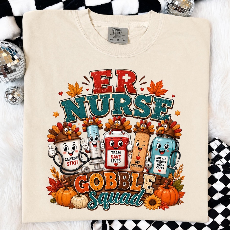May include: A cream-colored t-shirt featuring a graphic with the text ER NURSE GOBBLE SQUAD. The design includes cartoon characters like a coffee cup, syringe, blood bag, bandage, and medicine bottle, all wearing turkey hats, surrounded by autumn leaves.