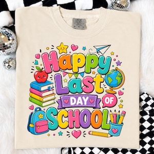 May include: A beige t-shirt featuring a colorful graphic with the text Happy Last Day of School. The design includes a stack of books with an apple, a globe, a blue backpack, pencils in a cup, a paper airplane, stars, and hearts in bright colors.