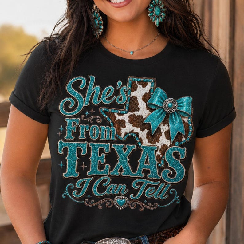 Puede incluir: Camiseta negra con el texto "She's From Texas I Can Tell". El dise&ntilde;o incluye un gr&aacute;fico en forma de Texas con un estampado de piel de vaca y un lazo turquesa. El texto y el lazo tienen un efecto brillante.
