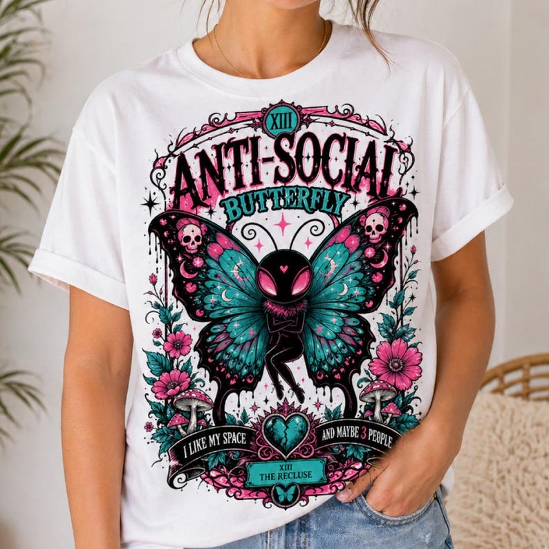 May include: White t-shirt with a graphic of a butterfly with teal and pink wings, skulls, and the text "ANTI-SOCIAL BUTTERFLY". The design includes flowers, mushrooms, and the phrases "I LIKE MY SPACE" and "AND MAYBE 3 PEOPLE".