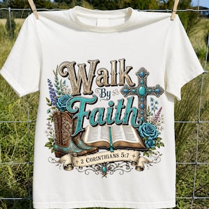 May include: A cream-coloured t-shirt featuring a graphic print with the text "Walk By Faith" and "2 Corinthians 5:7". The design includes a pair of brown and turquoise cowboy boots, an open book, a turquoise cross, and blue floral accents.