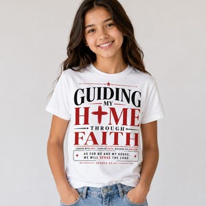 Peut inclure: T-shirt blanc avec le texte "GUIDING MY HOME THROUGH FAITH" en noir et rouge. Le t-shirt comprend &eacute;galement le verset biblique Josu&eacute; 24:15. La personne porte un jean bleu.