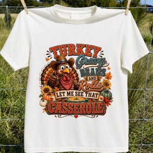 May include: A cream-colored t-shirt featuring a graphic of a turkey wearing a cowboy hat and a red bandana. The text reads: TURKEY Gravy BEANS AND Rolls LET ME SEE THAT CASSEROLE. The design includes sunflowers, pumpkins, and autumn leaves.