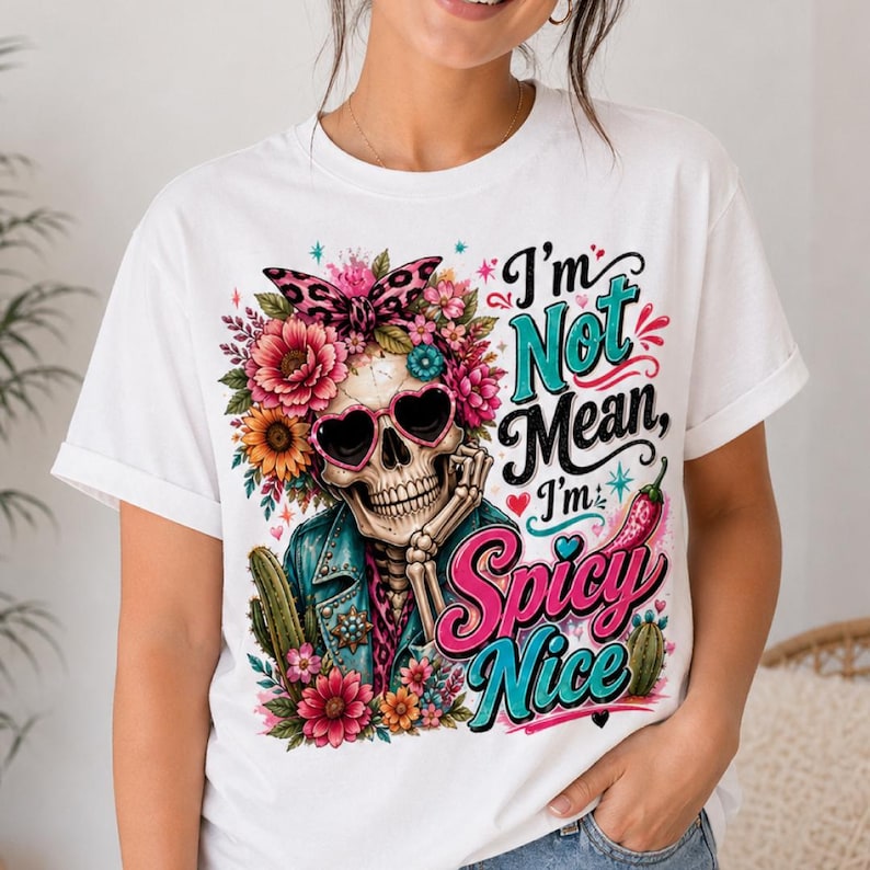 May include: White t-shirt featuring a colorful graphic of a skeleton wearing heart-shaped sunglasses and a floral crown. The text reads "I'm Not Mean, I'm Spicy Nice" in turquoise and pink. The skeleton is wearing a blue jacket.