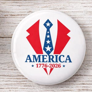 May include: A white button with a patriotic design. It features a red and blue graphic of a suit jacket and tie, with the word "AMERICA" and the years "1776-2026" in blue.