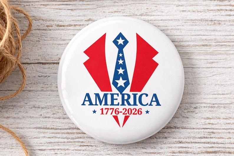 May include: A white button with a patriotic design. It features a red and blue graphic of a suit jacket and tie, with the word "AMERICA" and the years "1776-2026" in blue.