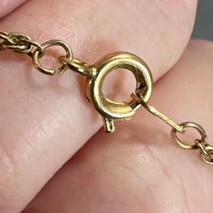 May include: Close-up of a gold-colored necklace clasp and chain. The clasp is a round, spring-ring type, and the chain is a delicate, twisted design. The clasp is attached to a portion of the chain.