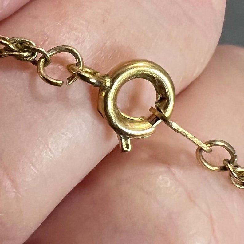 May include: Close-up of a gold-colored necklace clasp and chain. The clasp is a round, spring-ring type, and the chain is a delicate, twisted design. The clasp is attached to a portion of the chain.
