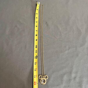 May include: A gold-colored necklace with a Mickey Mouse pendant. The pendant is approximately 1.5 inches wide and 1.25 inches tall. The chain is about 15 inches long. The pendant has a clear, sparkly design inside the Mickey Mouse head.
