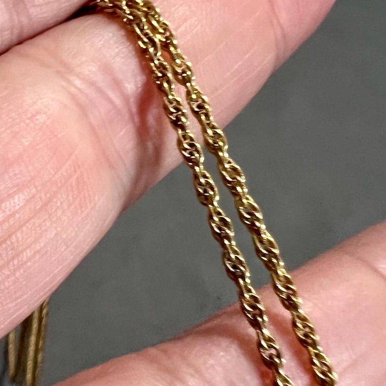 May include: Close-up of two gold-colored rope chains. The chains are intertwined and appear to be made of a shiny, metallic material. The background is a blurred, neutral color.