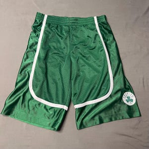 May include: Green basketball shorts with white trim and a mesh design. The shorts feature the Boston Celtics logo on the lower right leg. The shorts are made of a shiny, athletic material.
