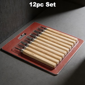 Puede incluir: Un juego de 12 piezas para tallar madera. Las herramientas tienen mangos de madera de color claro y collares de metal plateado. Las cuchillas son oscuras y anguladas. El juego está empaquetado en un blíster de plástico transparente sobre un respaldo de cartón rojo.