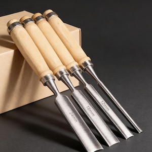 Può includere: Un set di quattro scalpelli in legno con manici in legno e lame in metallo. Le lame sono contrassegnate con le dimensioni: 24 mm, 18 mm e 12 mm. Gli scalpelli sono disposti in fila.