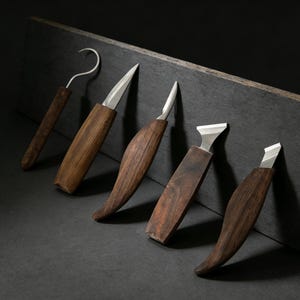 May include: A set of five wood carving tools with stainless steel blades. The handles are made of dark brown wood. One tool has a curved hook blade, while the others have various straight and angled blades.