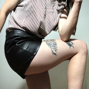 May include: A sleeveless top featuring a vertical brown and white striped pattern with a dark brown trim around the neckline and armholes, paired with black leather shorts that have a smooth finish and a visible seam along the front panel.
