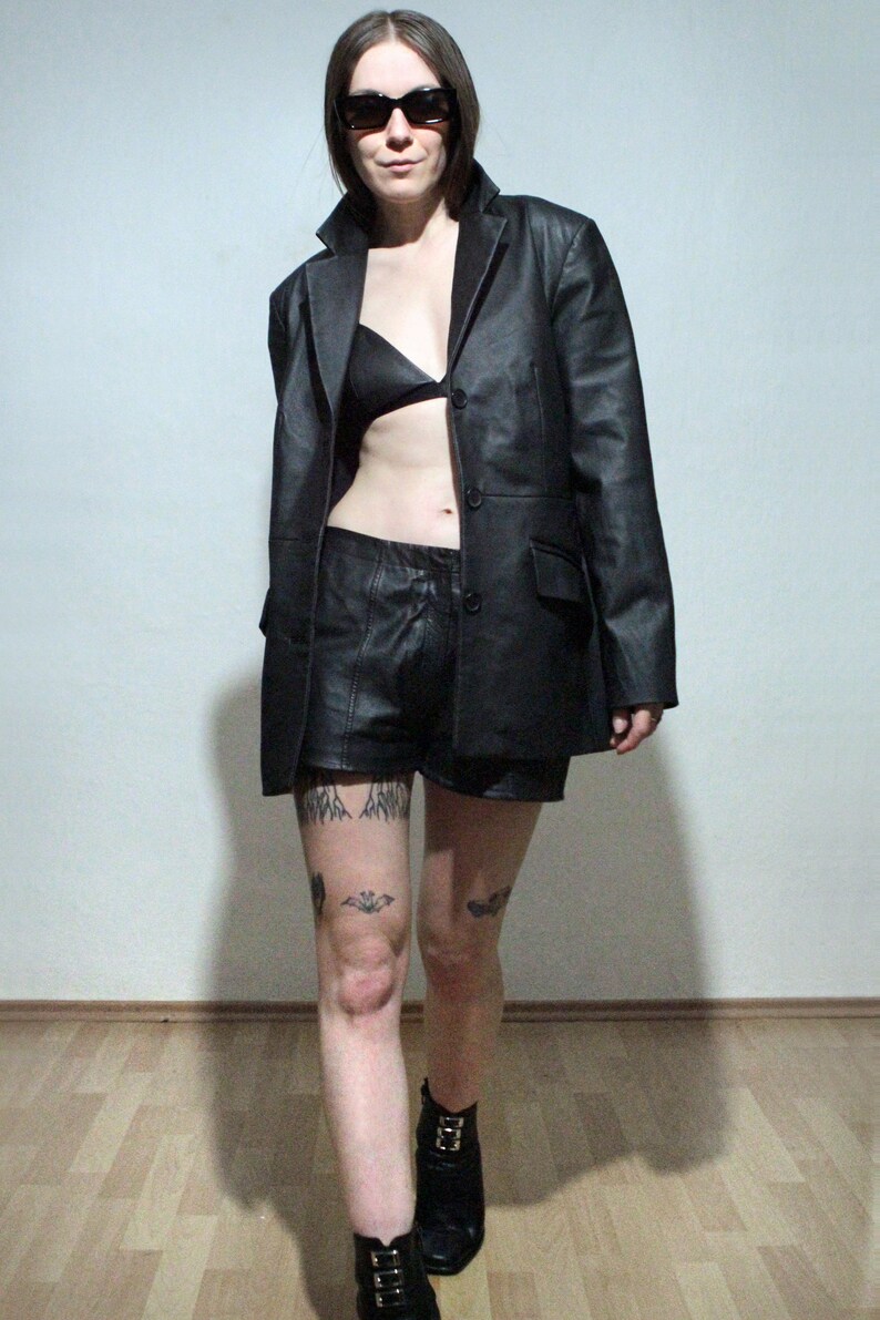 tattooed model wearing black leather blazer with leather bra high waisted leather shorts and ankle boots