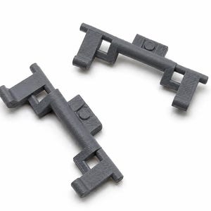 May include: Two identical dark gray plastic components with a textured surface. Each piece features a curved central bar, two rectangular cutouts, and small protruding tabs on the ends and sides, showing a layered 3D printed construction.