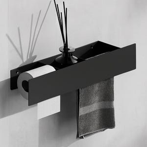May include: A matte black wall-mounted bathroom shelf featuring three distinct compartments. The left section holds a roll of white toilet paper, the center contains a black reed diffuser, and the right side holds a folded gray hand towel.
