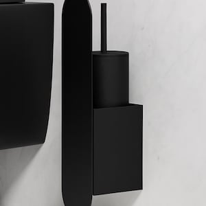 May include: A matte black wall-mounted toilet brush holder featuring a tall, vertical oval backplate and a square-shaped container. The cylindrical brush handle extends upward from the center of the circular lid, creating a sleek, uniform appearance.