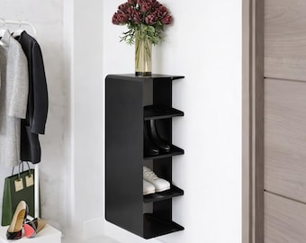 May include: A matte black wall-mounted storage unit with four open shelves. The top shelf holds a glass vase filled with dark red flowers. The lower shelves contain a pair of black boots and a pair of white sneakers. The unit has a curved side.