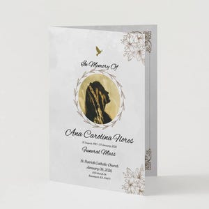 Può includere: Un programma funebre bianco con una silhouette in una cornice circolare, decorazioni floreali e il testo "In Memory Of Ana Carolina Flores Funeral Mass". Il programma è piegato.