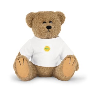 Könnte beinhalten: Ein brauner Plüsch-Teddybär mit dunklen Augen und einer schwarzen Nase, der ein weißes T-Shirt trägt. In der Mitte des T-Shirts befindet sich eine kreisförmige Grafik einer gelben Zitrusfruchtscheibe mit dem Namen Sofia in grünen Buchstaben.