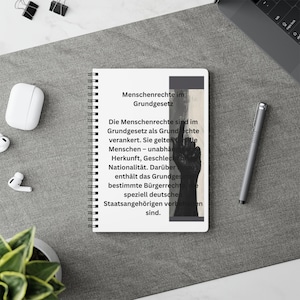 Könnte beinhalten: Ein Spiralnotizbuch mit weißem Einband und schwarzem Text: Menschenrechte im Grundgesetz. Die Menschenrechte sind im Grundgesetz als Grundrechte verankert. Sie gelten für alle Menschen – unabhängig von Herkunft, Geschlecht oder Nationalität. Darüber hinaus enthält das Grundgesetz bestimmte Bürgerrechte, die speziell deutschen Staatsangehörigen vorbehalten sind. Eine dunkle, silhouettierte Handgrafik ist auf der rechten Seite der Seite abgedruckt.