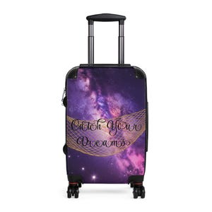 Könnte beinhalten: Ein Rollkoffer mit einem violett-rosa Galaxie-Druck und einem goldenen Netz-Grafik-Overlay. Der Text Catch Your Dreams ist in schwarzer Schreibschrift in der Mitte aufgedruckt. Der Koffer hat einen schwarzen Rahmen, Griff und vier Rollen.