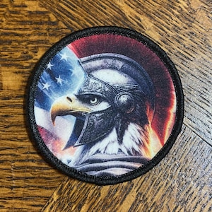 Pode incluir: Remendo redondo com uma águia com capacete em um fundo da bandeira americana. O remendo tem uma borda preta e mostra cores patrióticas, ideal para roupas e acessórios.